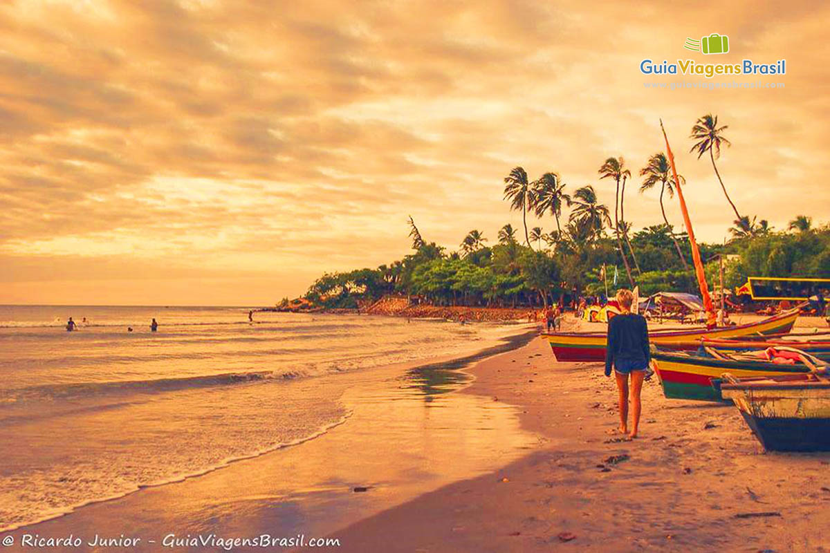 Imagem de turistas andando na frente dos barcos no entardecer na Praia Jericoacoara.